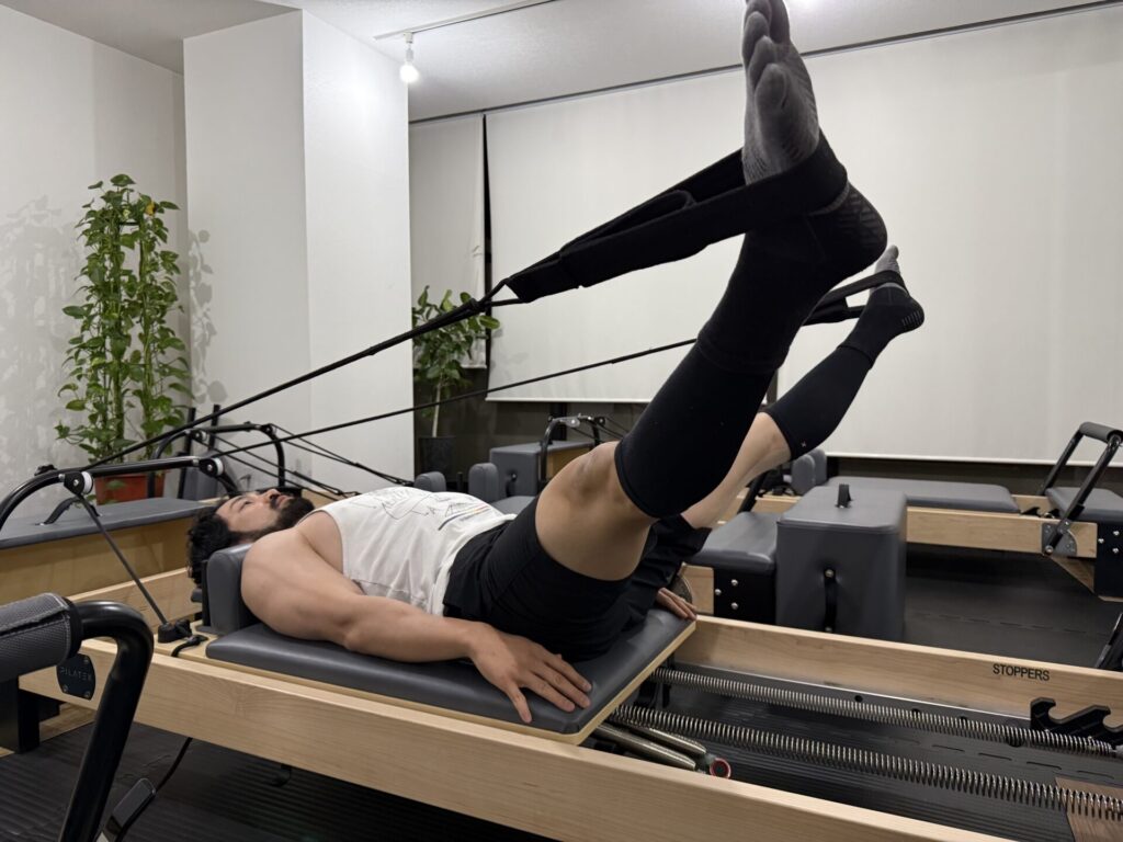 ボディビルダーがマシンピラティス（リフォーマー）で股関節のストレッチをしている様子。FILLNESSオーナー梅木